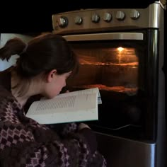 a woman reading a book in front of an oven