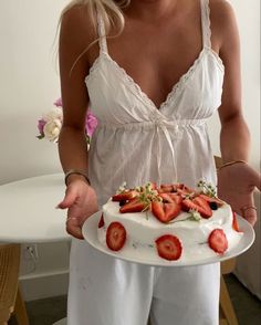 a woman holding a cake with strawberries on it