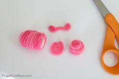 some pink crocheted items are sitting next to a pair of orange handled scissors