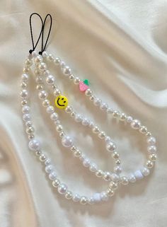 three necklaces with smiley face charms hanging from them on a white satin fabric background