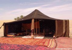 a tent set up in the desert with rugs and pillows on it's sides