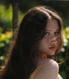 a woman with long brown hair and blue eyes is looking off into the distance while standing outside