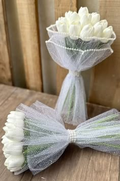 two white tulips wrapped in netting and tied with ribbon on a wooden table