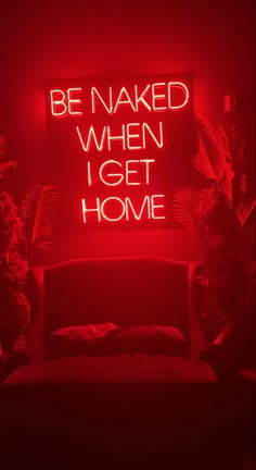 a red neon sign that says be naked when i get home in front of a couch