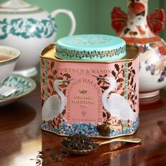 two tea tins sitting on top of a table next to cups and saucers