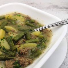 a white bowl filled with green beans and meat next to a spoon on top of a table