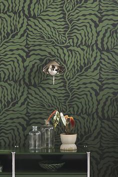 a green and black wallpaper with an animal print pattern on the side table next to vases