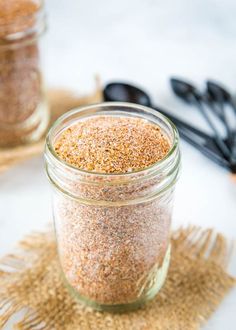 two jars filled with different types of spices on top of a table next to utensils