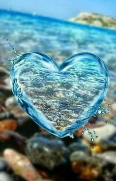 a heart shaped object floating on top of water surrounded by rocks and pebbles, with the ocean in the background