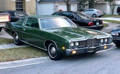 a green car parked on the side of a road next to other cars in front of a house