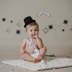 a baby in a top hat and diaper is sitting on a blanket with confetti