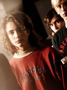 three young men standing next to each other in front of a wall wearing sweaters