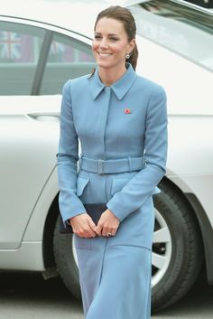 a woman in a blue coat and dress standing next to a car