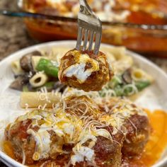 a fork is lifting up some meatballs from a plate with pasta and sauce on it