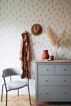 a room with a chair, coat rack and hat on the wall next to a dresser