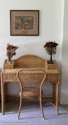 a wicker desk with two vases sitting on top of it next to a painting