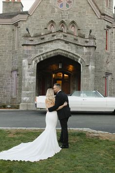 a bride and groom standing in front of an old church with a white car behind them