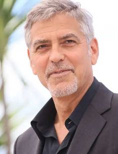 an older man with grey hair and beard wearing a black shirt, blazer and dark pants