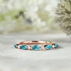 a rose gold ring with turquoise stones and diamonds on the side, sitting next to a pine tree