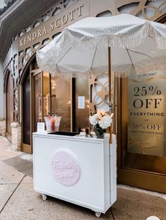 a white cart sitting in front of a store with an umbrella over it's top