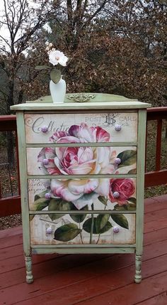 an old dresser with flowers painted on the front and side drawers is sitting on a deck