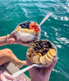 two people are holding up desserts in their hands on the water's edge