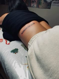 a woman laying on top of a bed with a tattoo on her arm that reads born to god