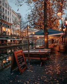 an empty street with tables and benches next to water in the middle of it at dusk