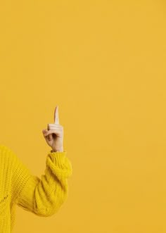 a woman in a yellow sweater is holding her hand up to the side and pointing at something