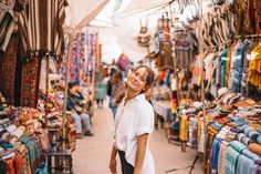 a woman standing in front of a market filled with cloths