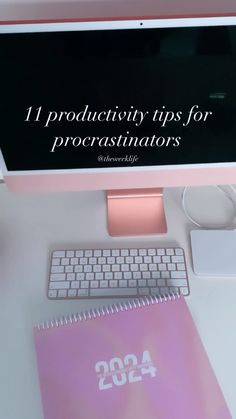 a desktop computer sitting on top of a desk next to a pink notebook and keyboard