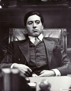 a man sitting in a chair wearing a suit and tie