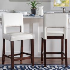 two white bar stools sitting in front of a kitchen counter