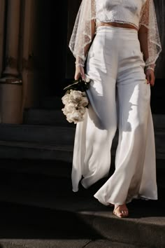 a woman is walking down the street in white pants and a crop top with sheer sleeves