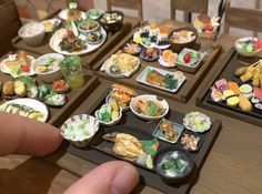 a person is pointing at small trays of food on the table with chopsticks