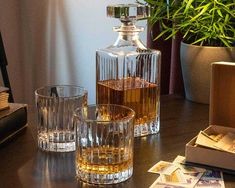 three glasses and two bottles on a table with money in front of them, next to a plant