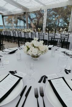 a table set with black and white place settings, silverware and flowers in a vase