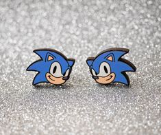 two sonic the hedgehog earrings are sitting on a silver glittered surface with sparkles in the background