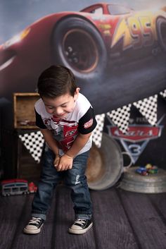 a young boy standing in front of a race car backdrop