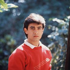 a young man in a red sweater is posing for a photo with trees in the background