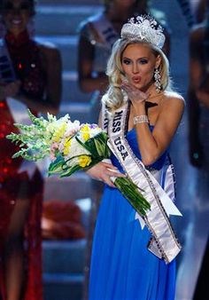 a woman in a blue dress is holding flowers and posing for the camera while wearing a tiara