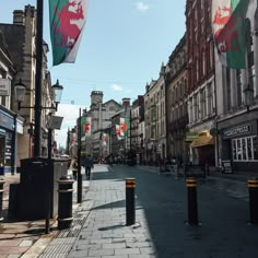 an empty city street with people walking on the sidewalk and flags flying in the air