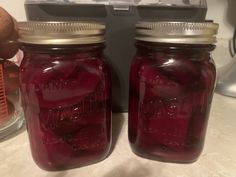 two jars filled with pickles sitting on top of a counter next to an egg