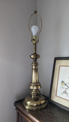 an antique brass lamp on a wooden table next to a framed photograph and small bird