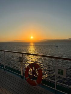 the sun is setting over the ocean on a boat deck with life preserver in foreground