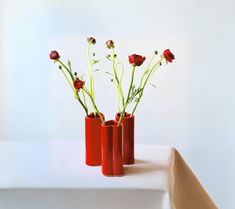 three red vases with flowers in them on a table