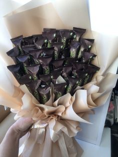 a hand holding a bouquet of chocolates wrapped in brown paper and tied with ribbon