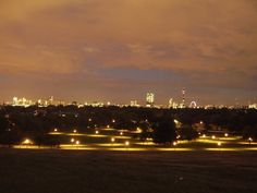 the city skyline is lit up at night with bright lights in the grass and trees