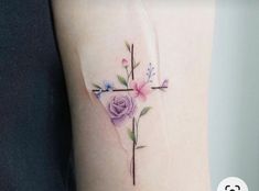 a cross with flowers on the side of her leg and behind it is a pink rose