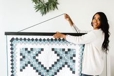 a woman holding up a quilt hanging on a wall